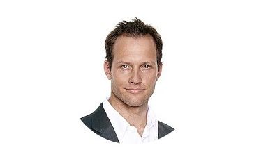 Dr. Lukas Brandner in dunklem Sakko und weißem Hemd blickt freundlich in die Kamera, vor einem weißen Hintergrund.
