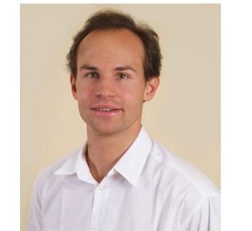 Dr. Matthias Wlk in weißem Hemd lächelt dezent vor einem beigen Hintergrund.