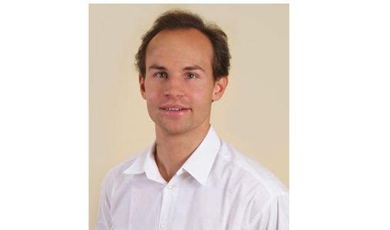 Dr. Matthias Wlk in weißem Hemd lächelt dezent vor einem beigen Hintergrund.