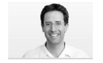 Schwarz-Weiß-Porträt von Dr. Helge Noske in weißem Hemd und Brille, lächelnd vor einem schlichten Hintergrund.