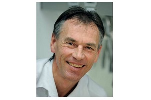 Dr. Harald Boszotta in weißem Arztkittel lächelt freundlich, im Hintergrund eine unscharfe medizinische Praxisumgebung.