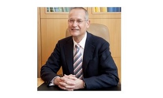 OA Dr. Georg Safoschnik in dunklem Anzug und gestreifter Krawatte sitzt lächelnd an einem Schreibtisch, im Hintergrund ein Bücherregal.